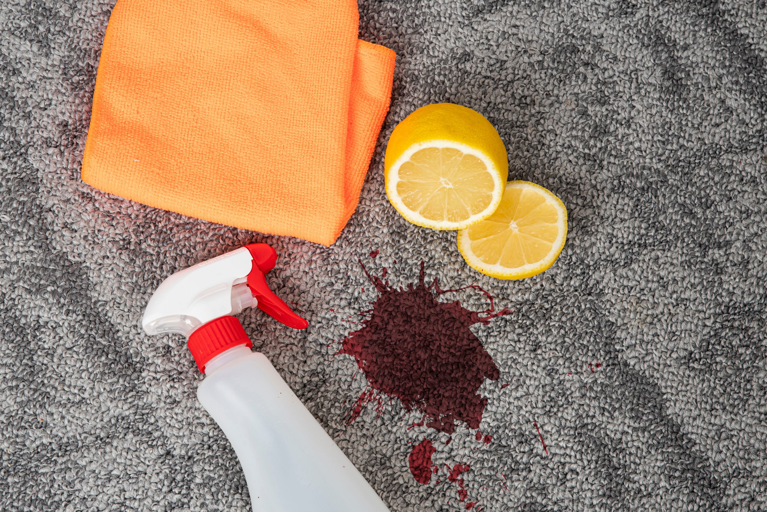 Dark stain, dirty spot on a carpeted floor, cleaning cloth, stain remover spray, Lemon for natural cleansing. Grey carpet needs cleaning and pollution removal.